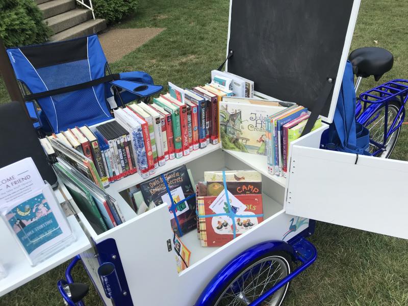 A book bike filled with books. A chair is nearby.