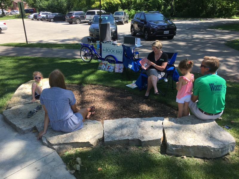 The Book Bike at Storytime in the Park. A woman reads a book to a group of children.