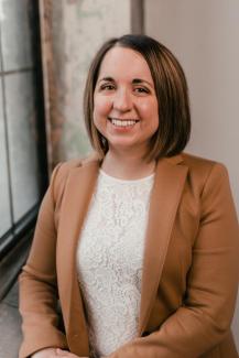 A woman in a brown blazer smiling.