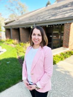 Photo of Library Director Renee Grassi standing in front of the Lake Bluff Public Library on a sunny day with clear skies and green grass.